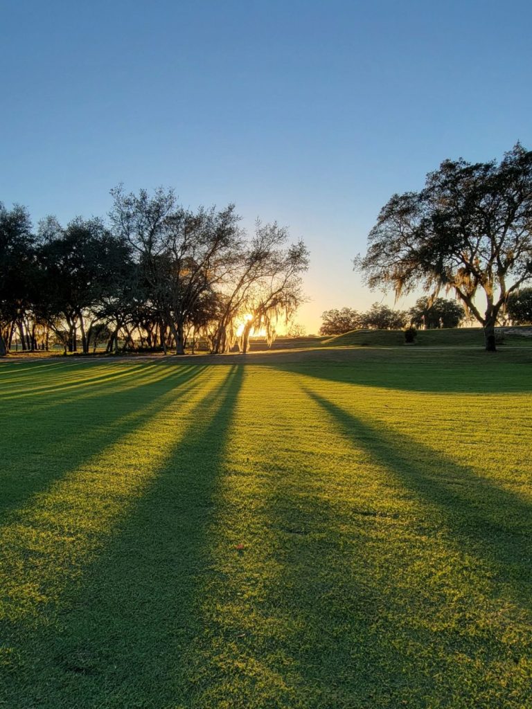 View of golf course with sunshine at sunrise through the trees